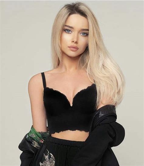 A Woman With Long Blonde Hair Wearing A Black Crop Top And Matching Gloves Is Posing For The Camera