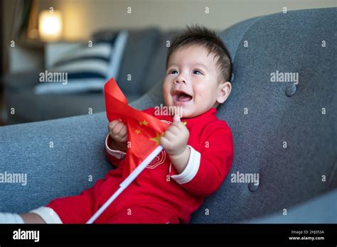 Asian Baby Boy Holding Chinese Flag Sitting On A Sofa While Wearing