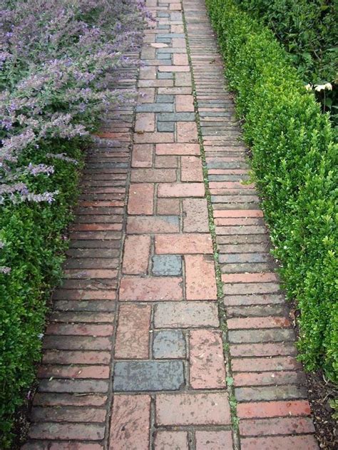 A Brick Path Between Two Rows Of Bushes And Flowers On Either Side Of