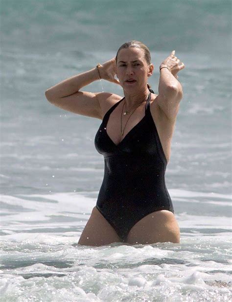 A Woman In A Black Swimsuit Standing In The Ocean With Her Hands On Her