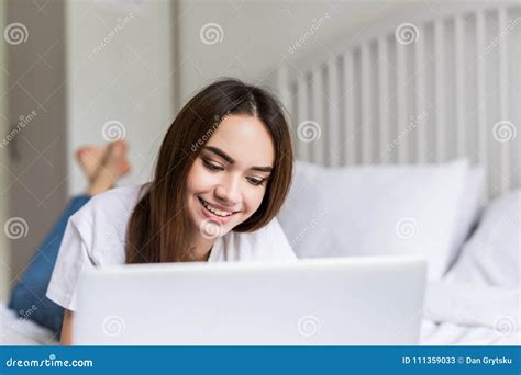 smiling woman catching up on her social media as she relaxes in bed with a laptop computer on a