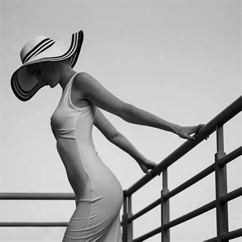 A Woman In A Dress And Hat Leaning On A Rail