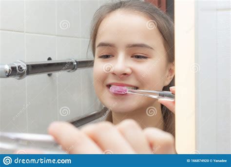 Health And Hygiene A Girl Brushes Her Teeth In Front Of A Mirror In