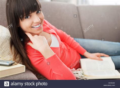 Beautiful Young Woman Relaxing At Home On The Sofa And Reading A Book She Is Smiling At Camera
