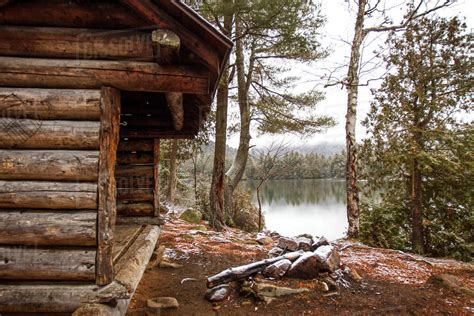 Old Log Cabin By Lake And Trees In Forest Stock Photo
