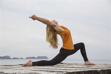 Mid Adult Woman Bending Backwards Practicing Yoga On Wooden Sea Pier