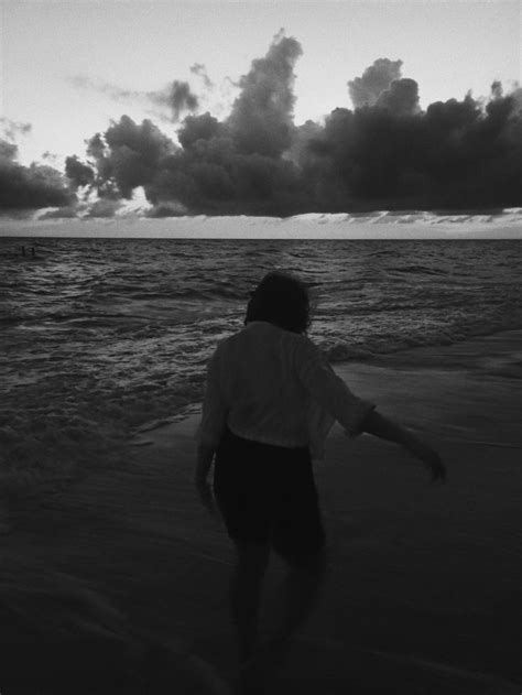 A Person Is Walking On The Beach In Front Of An Ocean With Dark Clouds Above