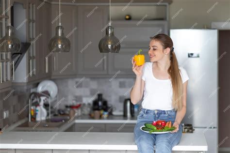 Ein Junges Mädchen Sitzt Am Küchentisch In Einer Modernen Küche Und Hält Gelbe Paprika Und Einen