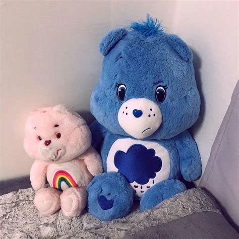 two teddy bears sitting on a bed next to each other and one is holding a rainbow heart