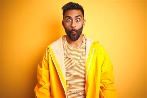 Young Indian Man Wearing Raincoat Standing Over Isolated Yellow