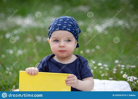 Baby Boy In A Blue Bandana On Head Sitting On The Green Grass Playing