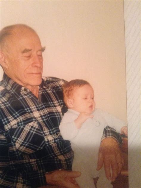 An Older Man Holding A Baby In His Lap And Looking At The Camera While Wearing A Plaid Shirt