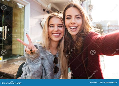 Two Joyful Attractive Girls Taking A Selfie While Sitting Together Stock Image Image Of