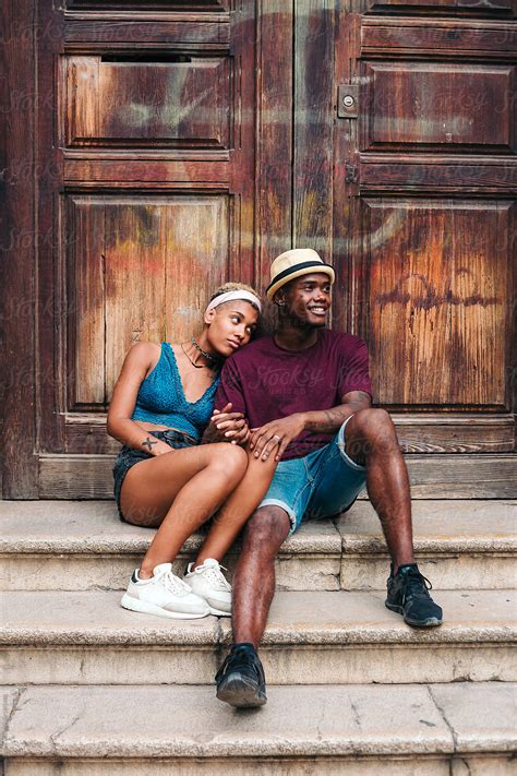 Young Multiracial Couple Sitting On A Doorstep By Lucas Ottone