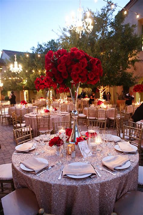 The Table Is Set With White Plates And Silverware Red Roses In Vases