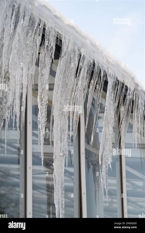 Icicles Hang From Roof And Wall In Winter Frozen Water From Melting