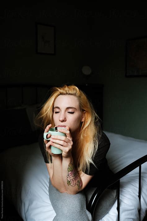 Sleepy Blonde Woman Sitting On The Bed Taking A Cup Of Coffee In The Morning By Stocksy