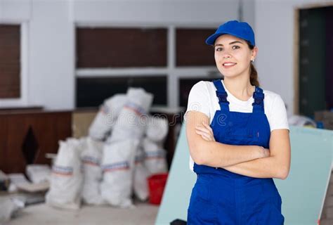 Portrait Of Contented Young Female Builder In Blue Overalls During The