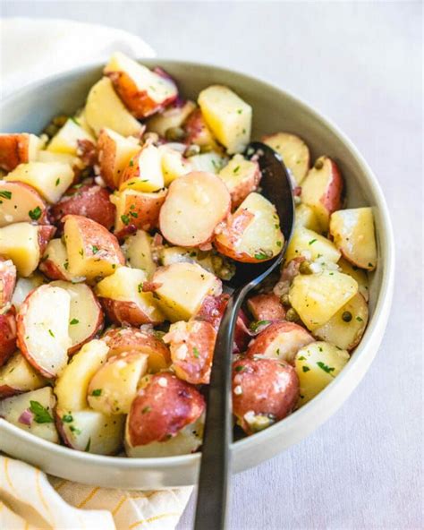 A Bowl Filled With Potatoes And Parsley On Top Of A White Cloth Next To