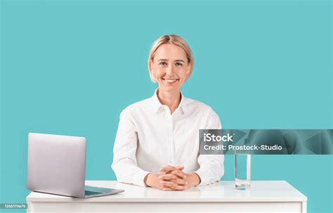 happy mature secretary sitting at her workplace with laptop computer on blue background stock