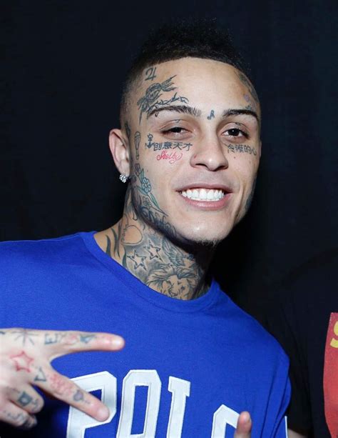 a man with tattoos and piercings on his face pointing at the camera while wearing a blue shirt