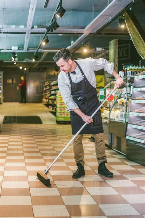 Full Length Of Salesman Sweeping Floor In Grocery Store Stock Photo