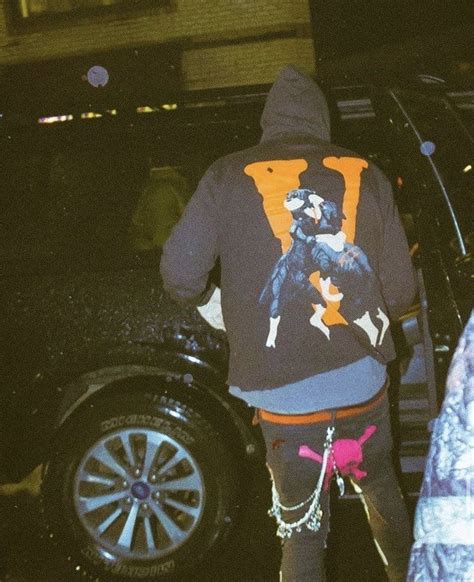 A Man In A Hoodie Is Walking Towards A Car With Chains On His Feet