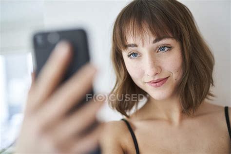 Portrait Of Smiling Young Woman Taking Selfie With Smartphone At Home