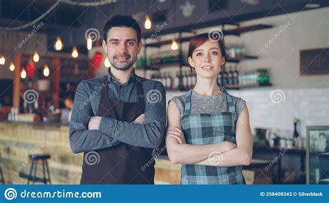 Portrait Of Two Cheerful Waiters Standing Inside Cozy Cafe Smiling And