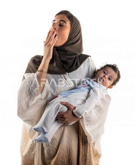 بورتريه لأم عربية خليجية سعودية تحمل طفلها الرضيع بحب وحنان، تضع يدها على فمها بإيماءات تدل