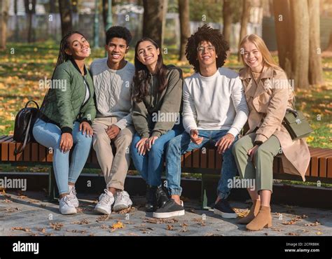 Group Of Positive Friends Sitting On Bench And Smiling Stock Photo Alamy