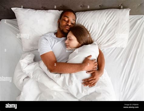 Top View Of Affectionate Multiracial Couple Hugging Each Other While Sleeping In Bed Stock Photo