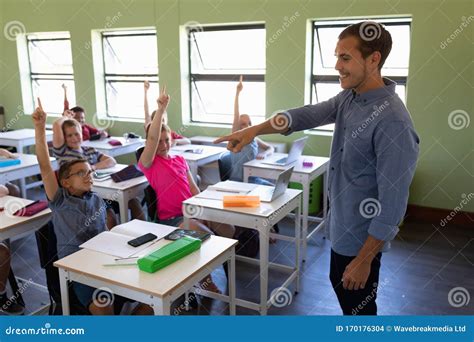 Male School Teacher Standing In An Elementary School Classroom With A