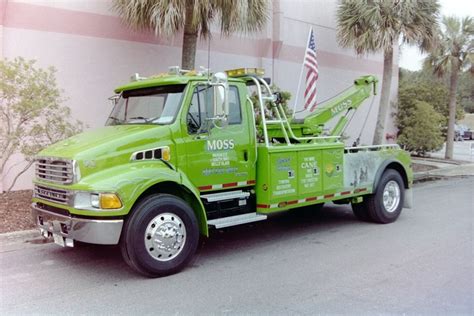 A Green Tow Truck Parked In Front Of A Building With Palm Trees On The Side