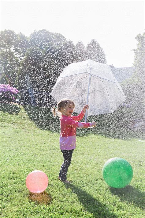Child Playing In Rain Umbrella In Colorful Spring Rainshower And Ball
