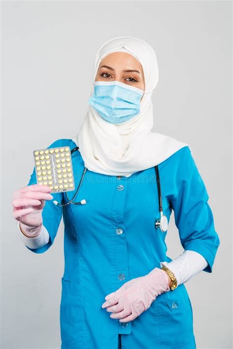 Friendly Muslim Doctor Or Nurse In A Hijab Mask Gloves Offering A Pill To The Patient On A