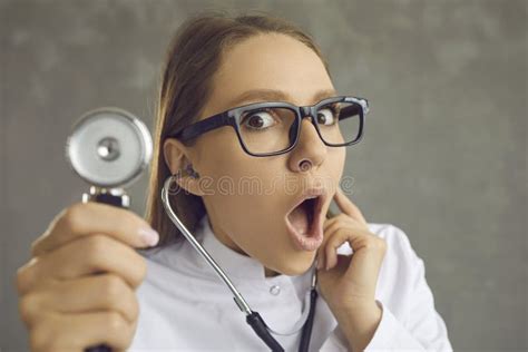 Shocked Female Doctor With A Surprised Face Raises A Stethoscope Listening To The Heartbeat