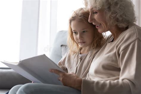 Close Up Smiling Mature Grandmother Reading Book To Granddaughter Stock