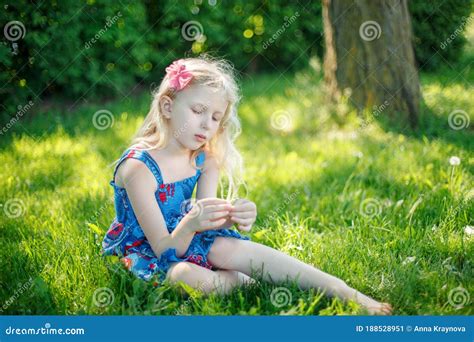 Pensive Young Girl In Blue Dress Sitting On Ground Outdoors On Summer
