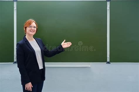 Happy Female Teacher Smiles Next To An Empty Blackboard Copy Space For