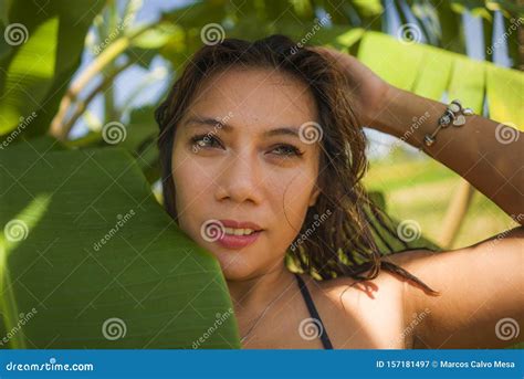 Young Beautiful And Happy Asian Indonesian Woman In Bikini Posing Between Leaves Of Banana Tree