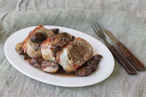 A White Plate Topped With Meat Covered In Mushrooms And Sauce Next To A