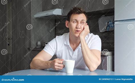 Sleepy Man Naps At Table And Drinks Cup Of Coffee In Kitchen Stock