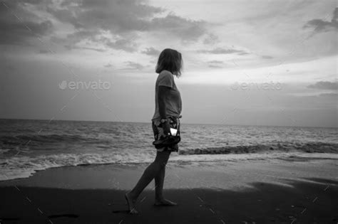 Grayscale Shot Of A Girl Standing On The Sandy Coast Of An Ocean