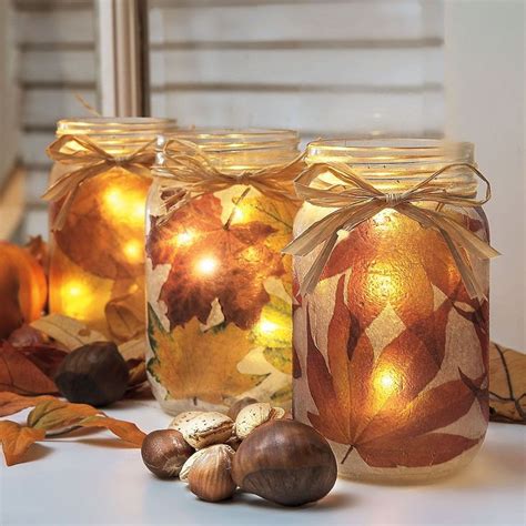 three mason jars with lights in them sitting on a table next to leaves and acorns