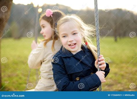 Two Adorable Young Girls Having Fun On A Swing Together In Beautiful