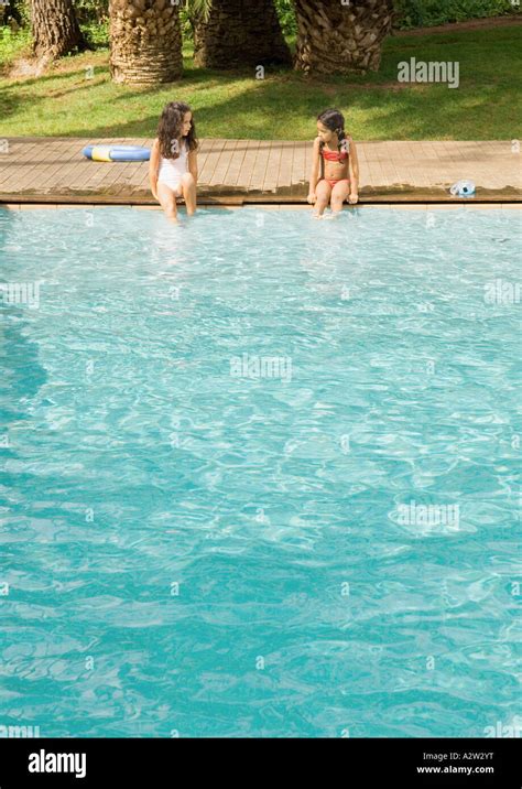 Two Girls Sitting On Edge Of Swimming Pool Stock Photo Alamy
