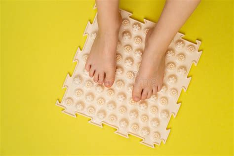 Childrenand X27s Feet On A Beige Orthopedic Mat On A Yellow Background