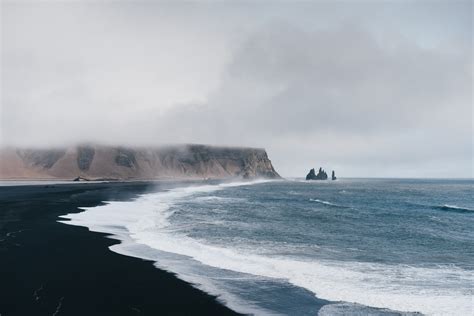 Black Sand Near Body Of Water Under The Cloudy Sky During