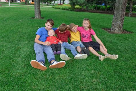 Five Children Are Sitting In The Park On The Green Grass Stock Photo